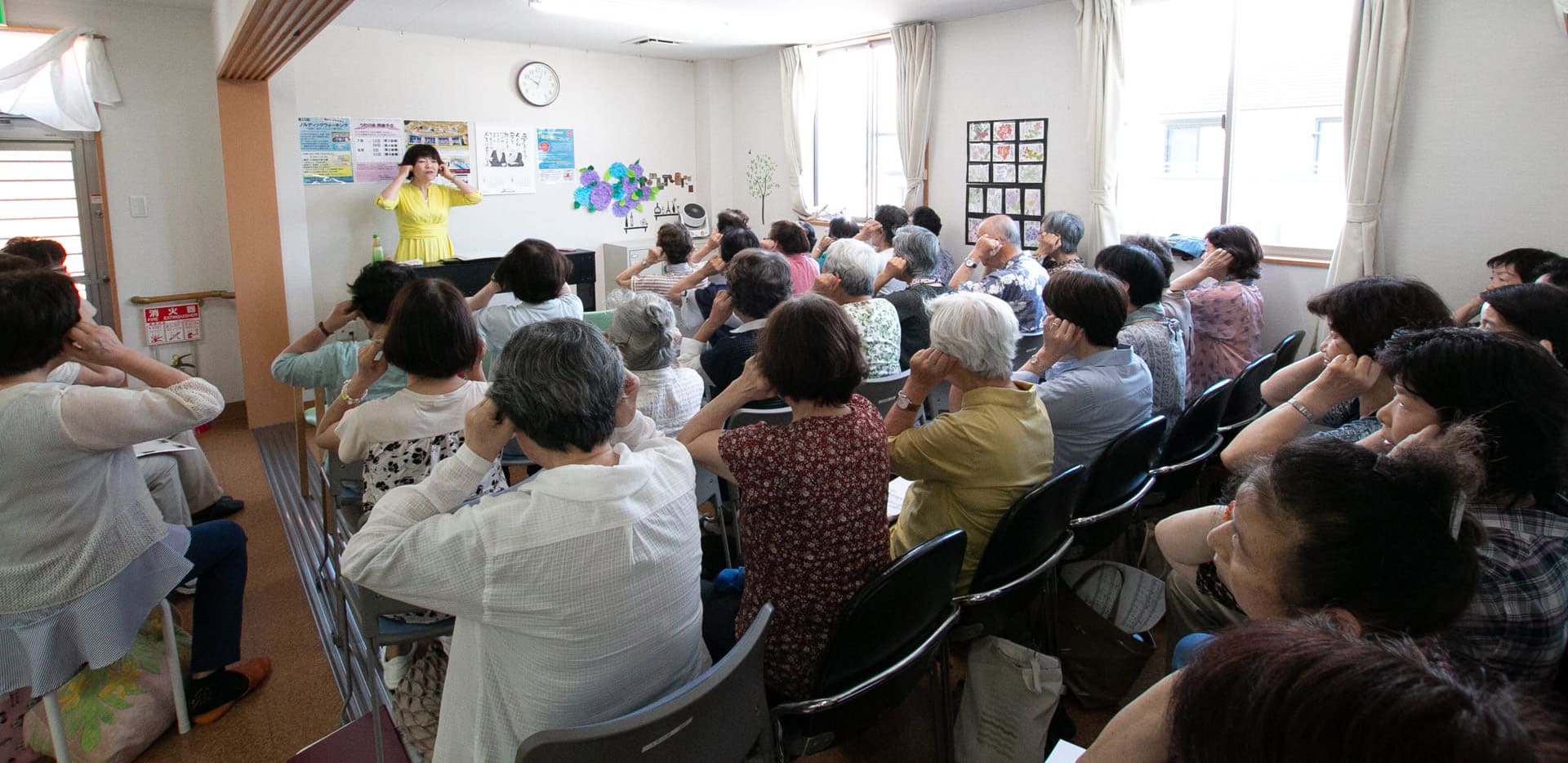 介護施設での集団レクリエーション。多数の高齢入居者が講師の指導を受けている風景。